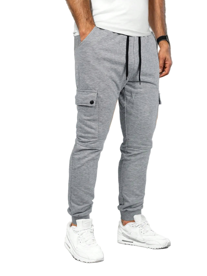 Person wearing gray jogger pants and white sneakers in a white background.