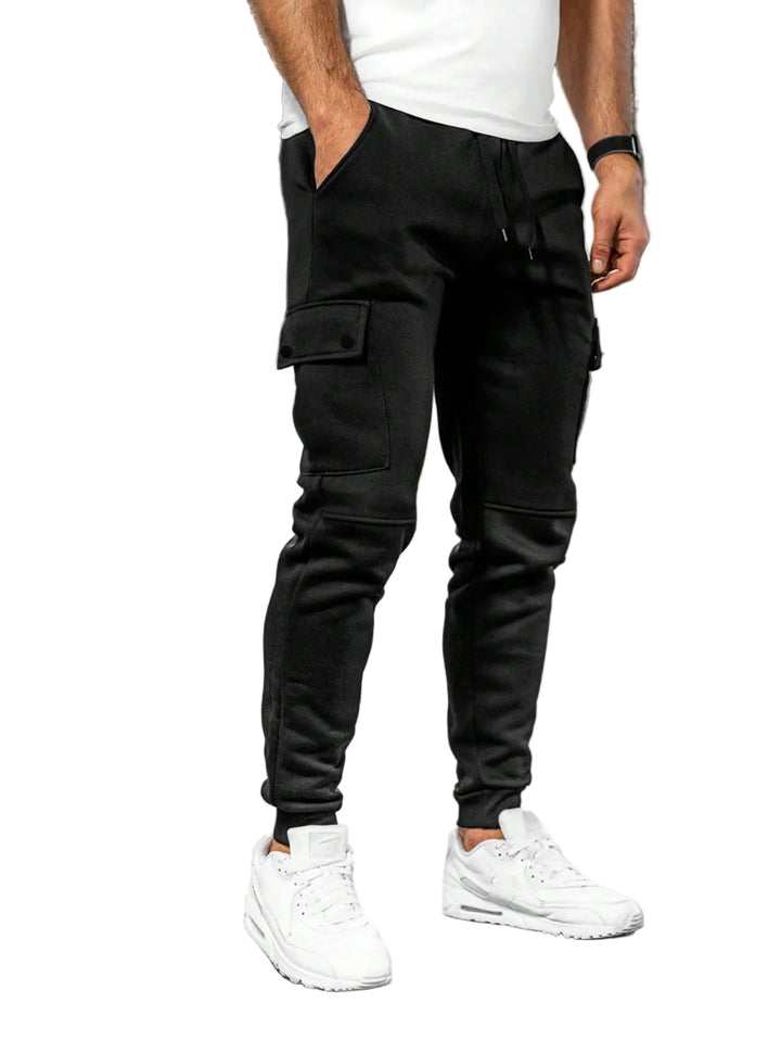 Person wearing black jogger pants and white sneakers in a white background.