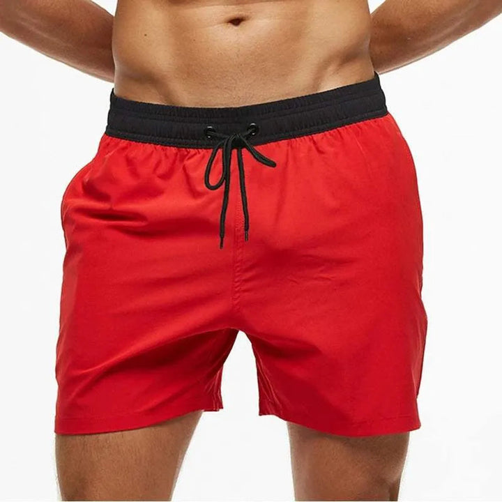 Red swim shorts with a black waistband on a white background