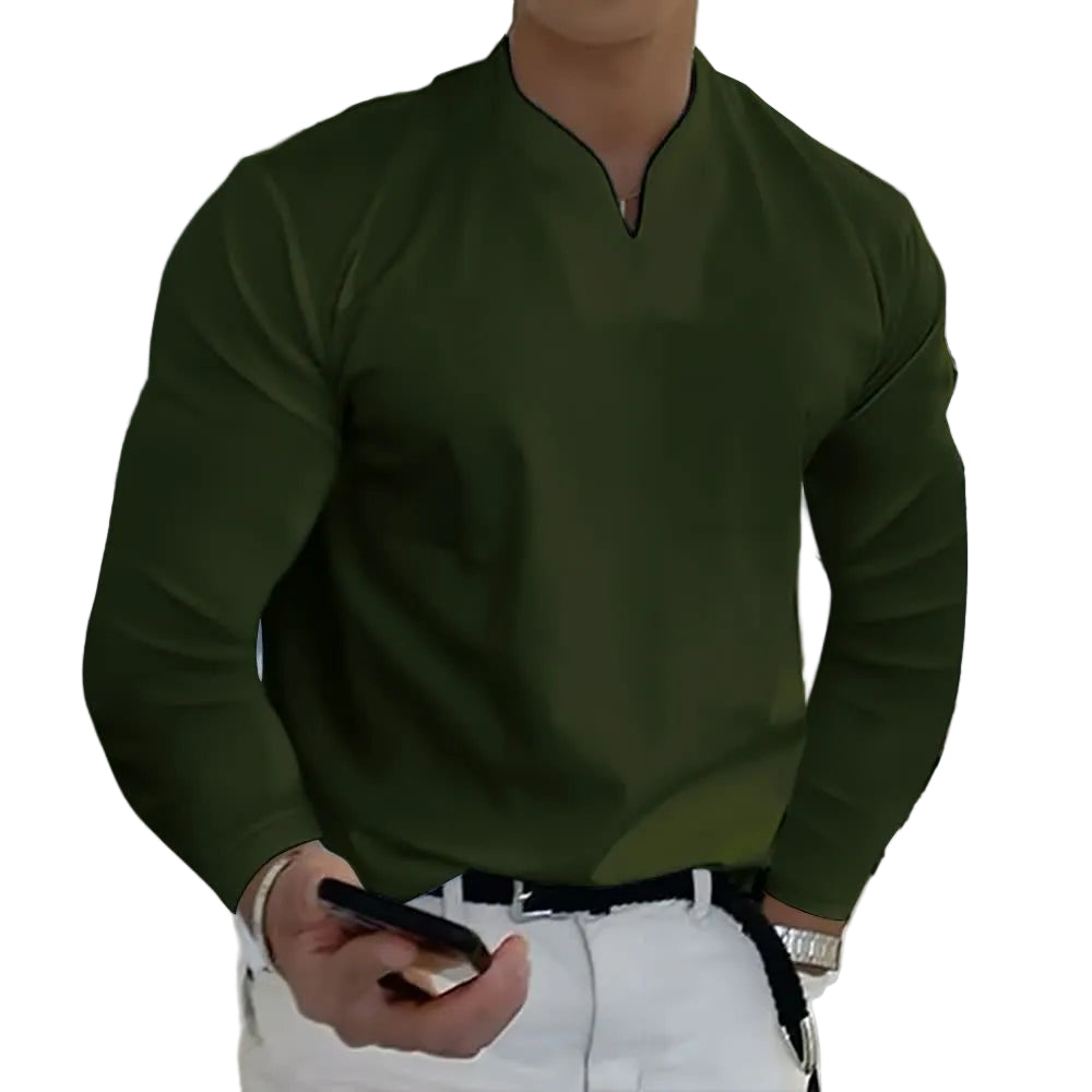 Person wearing a green sweater and white pants holding a phone, standing against a plain background.