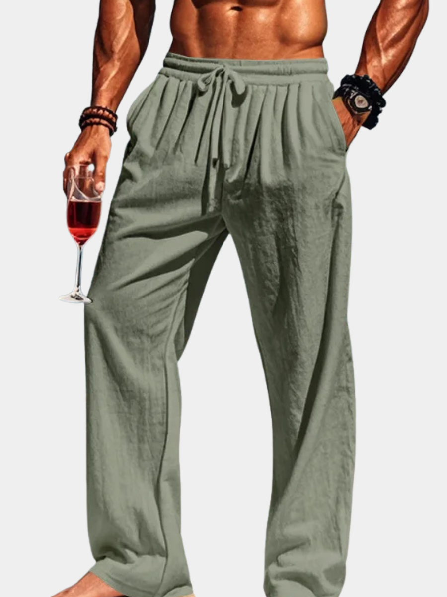 Person wearing olive green pants holding a glass of red wine on a plain white background