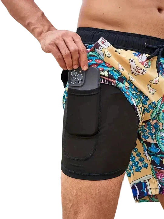 Person wearing colorful swim shorts with a black waistband, holding a phone case.