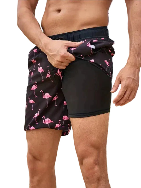 Person wearing black swim shorts with pink flamingo pattern on a white background.