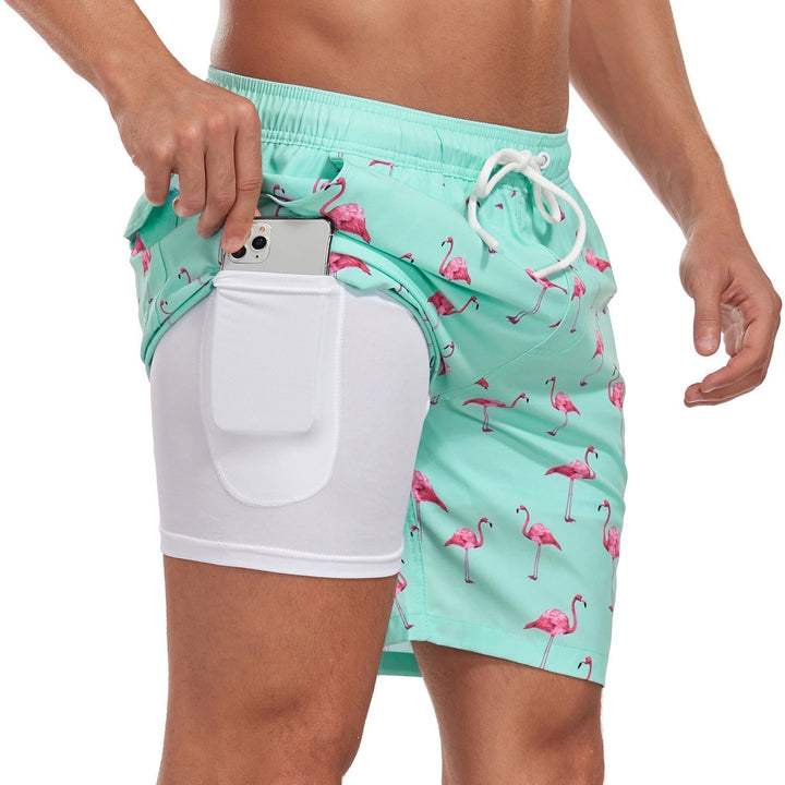 Turquoise swim shorts with flamingo pattern and white pocket held by a person on a white background