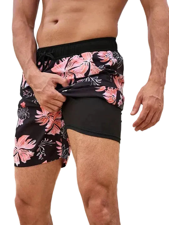Person wearing black swim shorts with pink floral pattern on a white background.