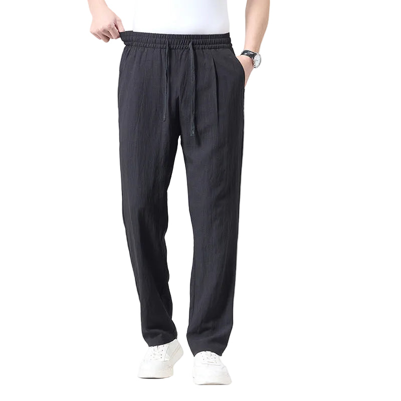 A person wearing dark charcoal gray drawstring pants, a white t-shirt, and white sneakers, shown from the waist down against a light white studio background.