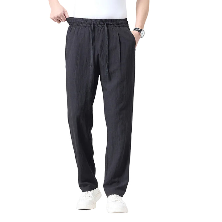 A person wearing dark charcoal gray drawstring pants, a white t-shirt, and white sneakers, shown from the waist down against a light white studio background.